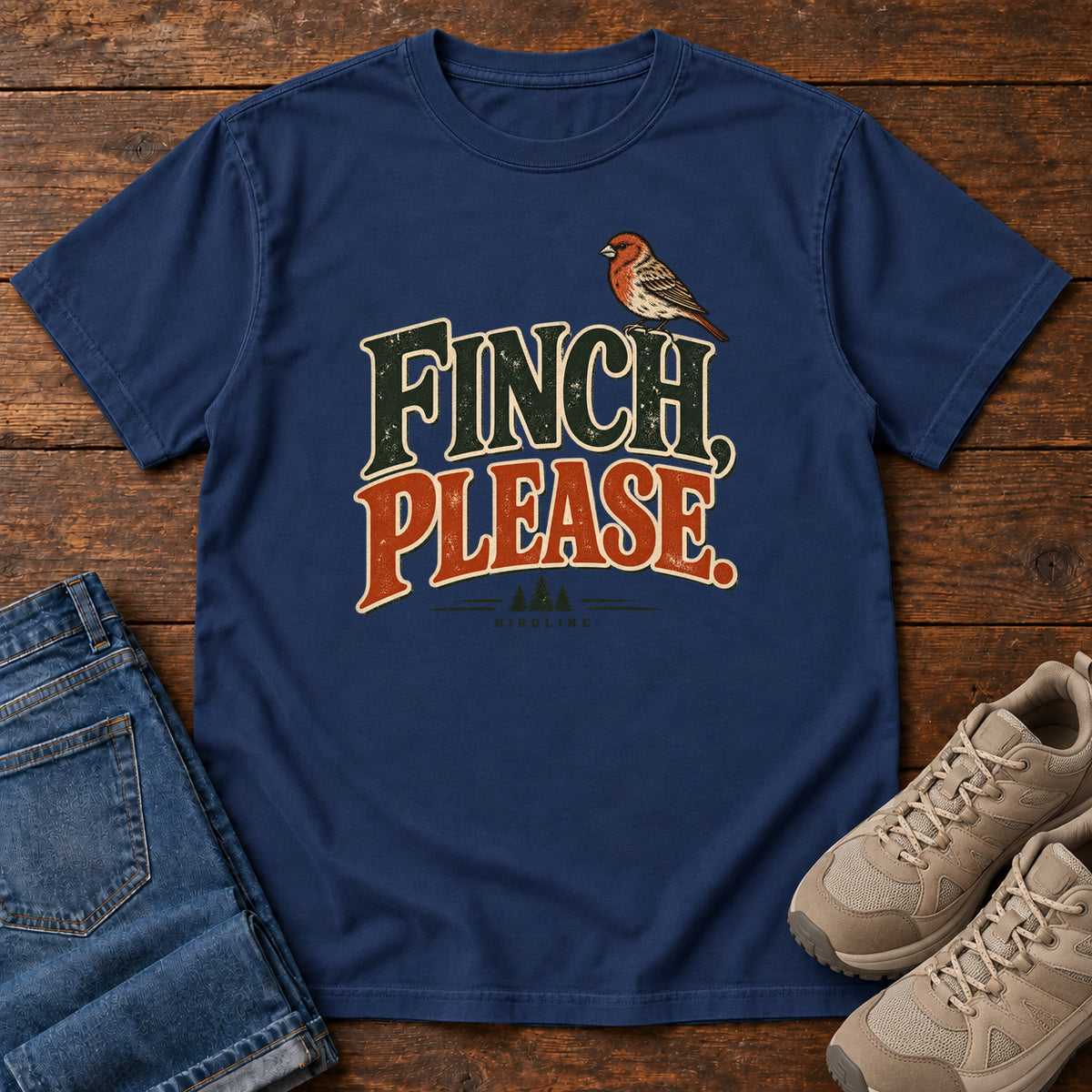 True Navy Finch, Please. T-Shirt with a small bird perched above cream-outlined green-and-orange lettering, front flat lay on wood.