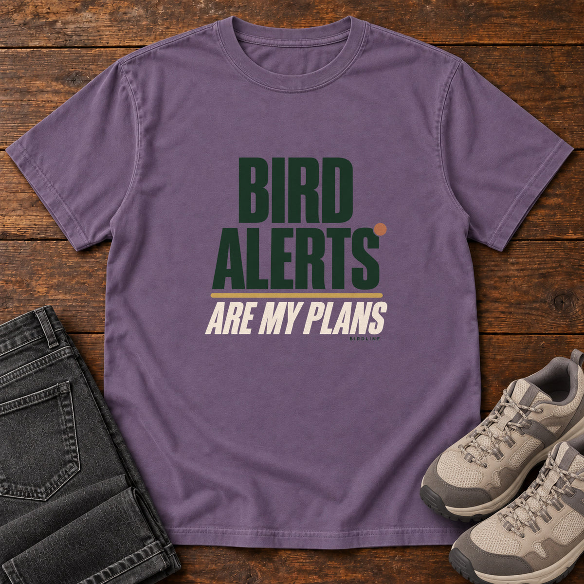 Grape Bird Alerts Are My Plans T-Shirt with stacked green-and-cream lettering and an orange accent; front flat lay on wood.
