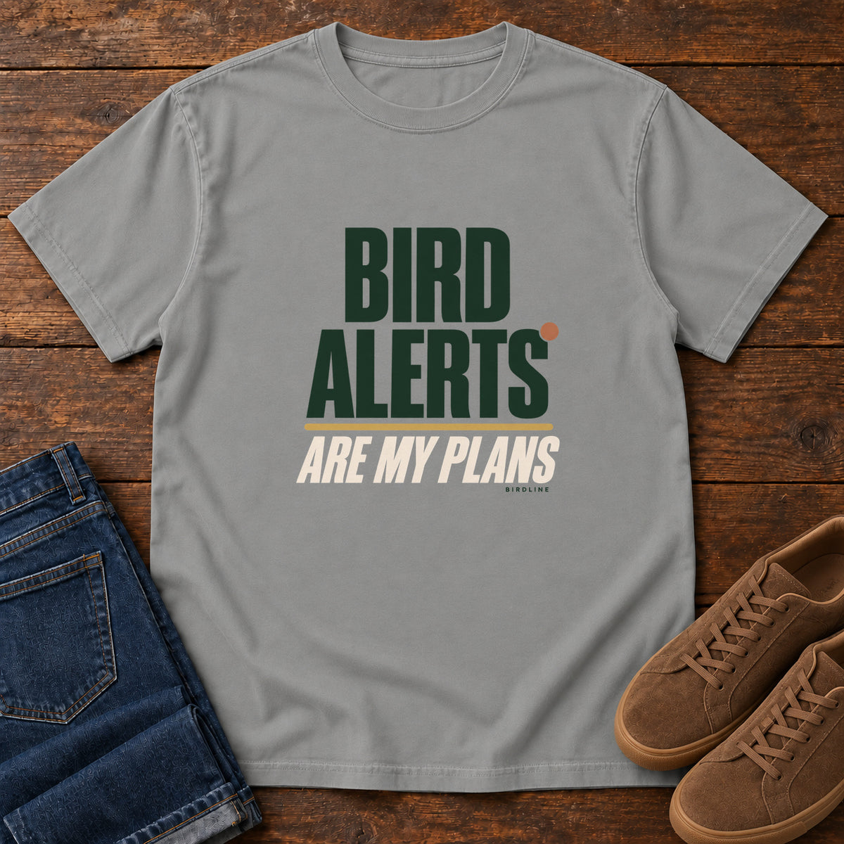 Grey Bird Alerts Are My Plans T-Shirt with stacked green-and-cream lettering and an orange accent; front flat lay on wood.