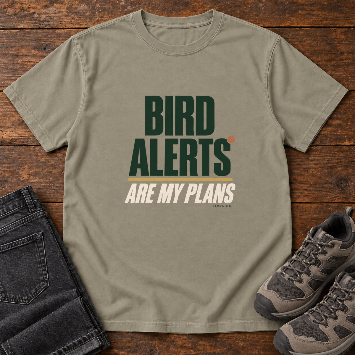 Sandstone Bird Alerts Are My Plans T-Shirt with stacked green-and-cream lettering and an orange accent; front flat lay on wood.