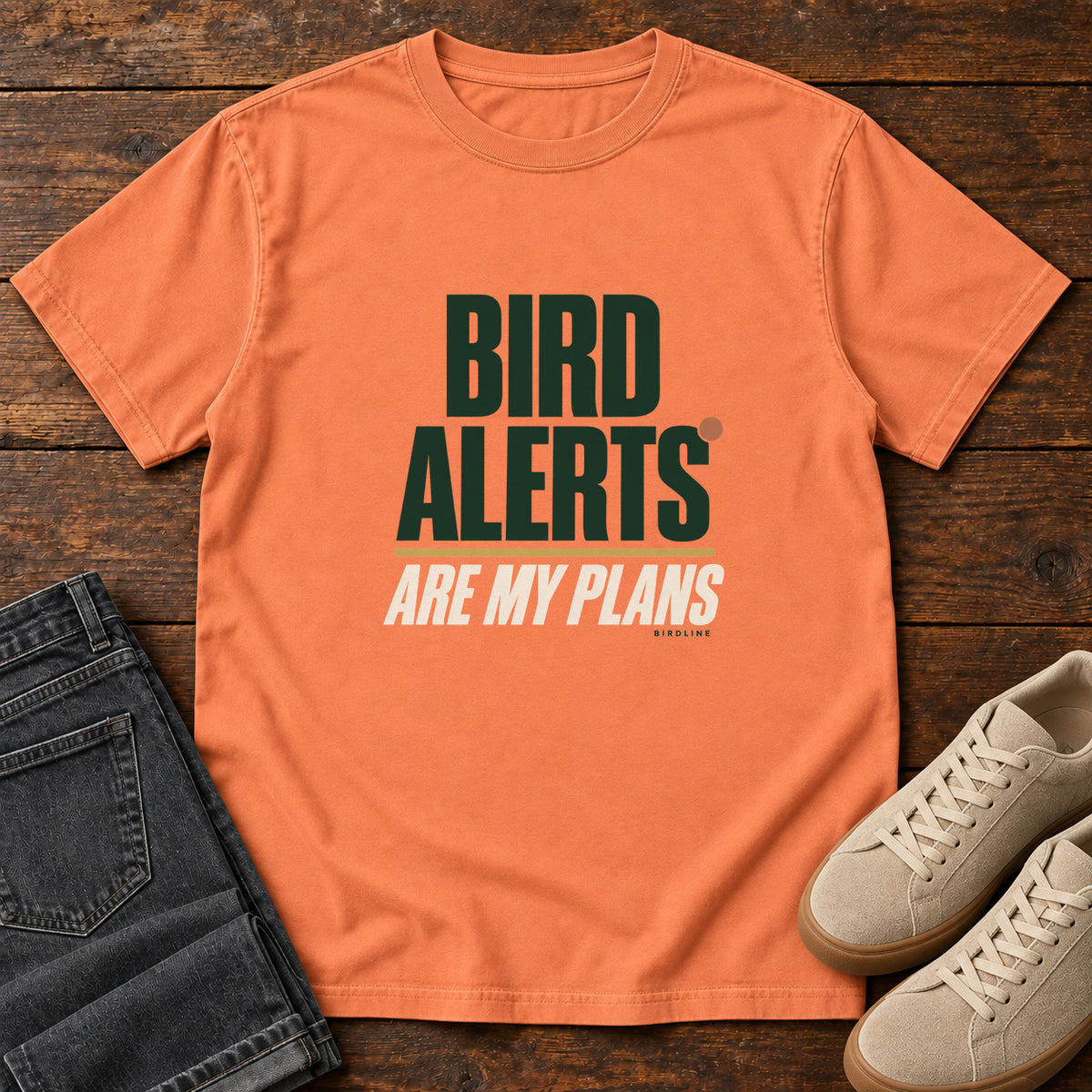 Terracotta Bird Alerts Are My Plans T-Shirt with stacked green-and-cream lettering and an orange accent; front flat lay on wood.