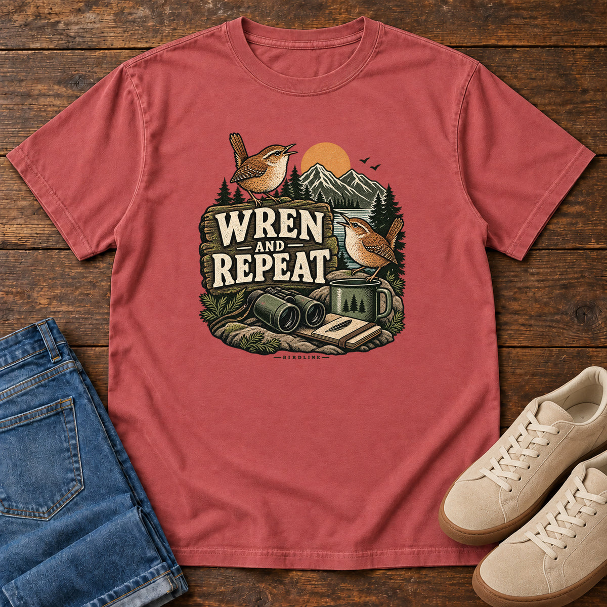 Crimson Wren and Repeat T-Shirt with two small brown birds, binoculars and a camp mug around Wren and Repeat lettering, front flat lay on wood.