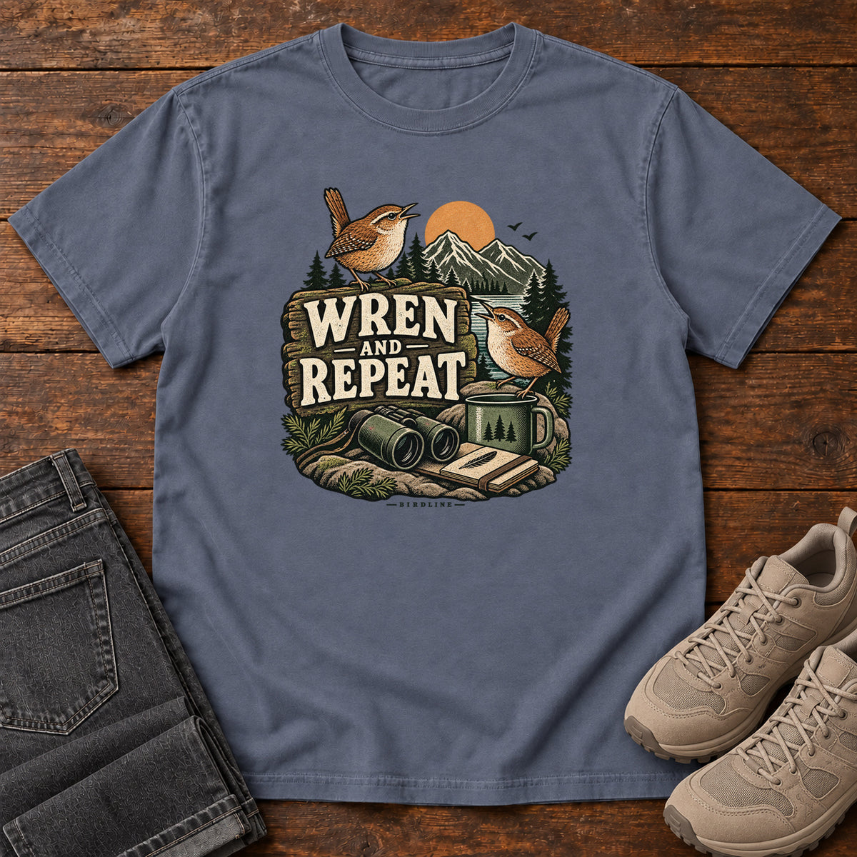 Denim Wren and Repeat T-Shirt with two small brown birds, binoculars and a camp mug around Wren and Repeat lettering, front flat lay on wood.