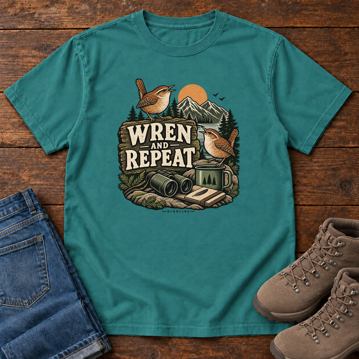 Emerald Wren and Repeat T-Shirt with two small brown birds, binoculars and a camp mug around Wren and Repeat lettering, front flat lay on wood.