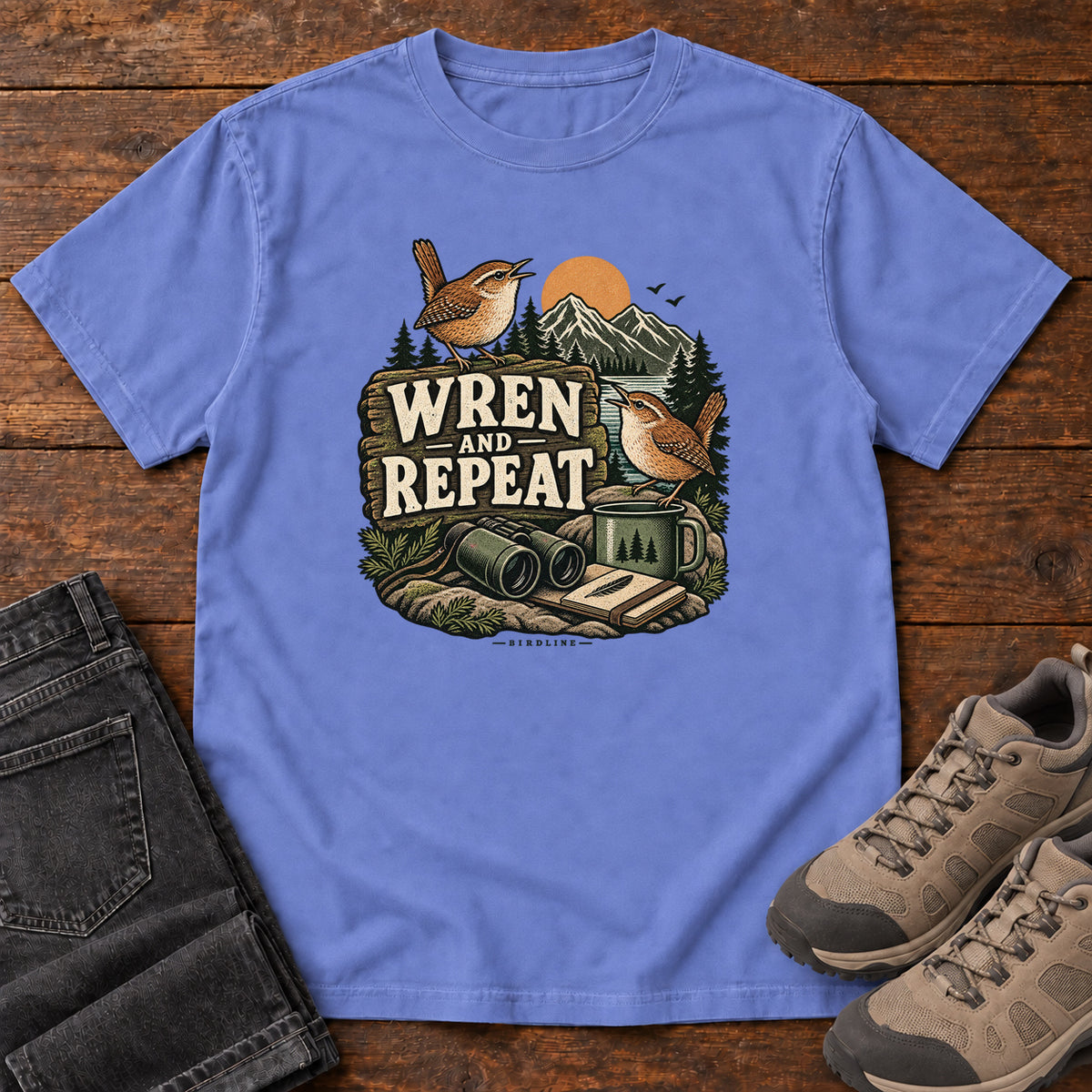Flo Blue Wren and Repeat T-Shirt with two small brown birds, binoculars and a camp mug around Wren and Repeat lettering, front flat lay on wood.