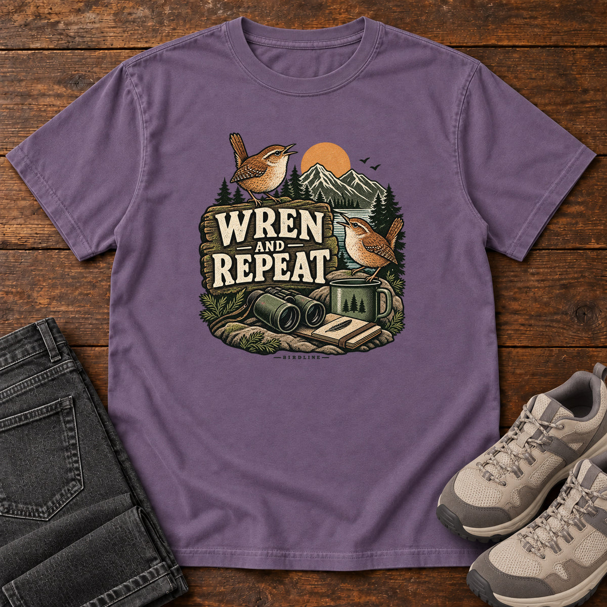 Grape Wren and Repeat T-Shirt with two small brown birds, binoculars and a camp mug around Wren and Repeat lettering, front flat lay on wood.