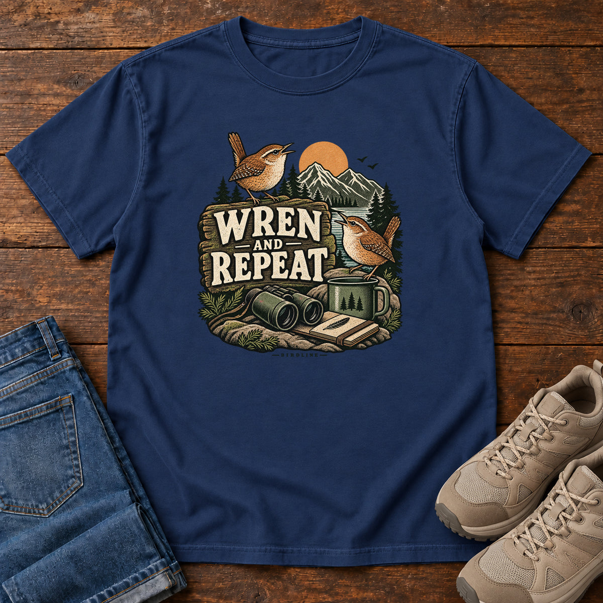 True Navy Wren and Repeat T-Shirt with two small brown birds, binoculars and a camp mug around Wren and Repeat lettering, front flat lay on wood.