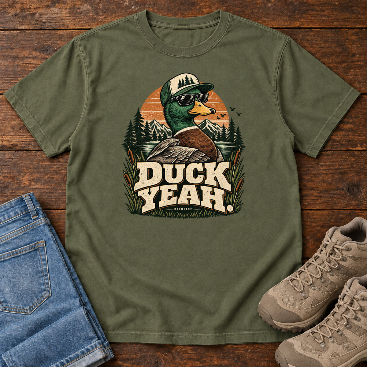 Hemp Duck Yeah T-Shirt with a green-headed duck wearing a cap and sunglasses above bold cream lettering, front flat lay on wood.