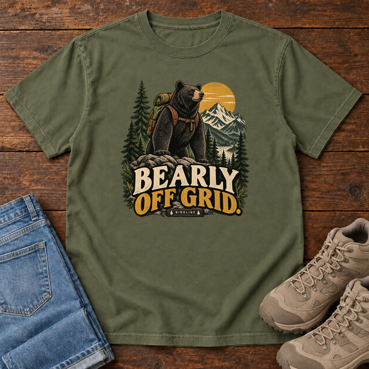 Hemp Bearly Off Grid T-Shirt with a black bear wearing a backpack before mountains, pines and a golden sun; front flat lay on wood.
