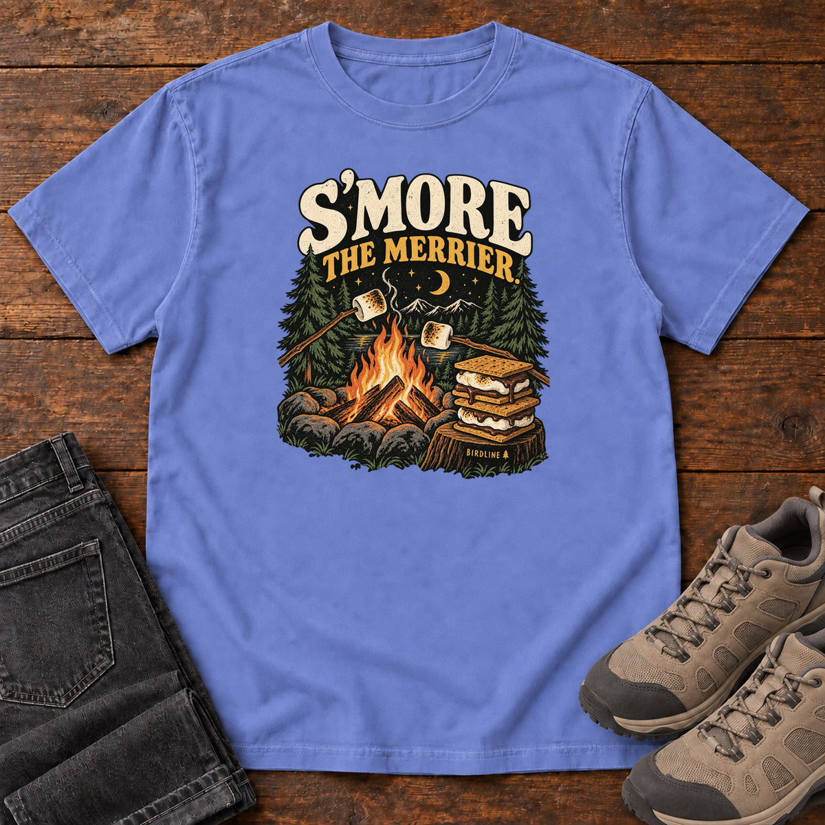 Flo Blue Smore the Merrier T-Shirt with a campfire, marshmallows on sticks and stacked s’mores beneath a crescent moon; front flat lay on wood.