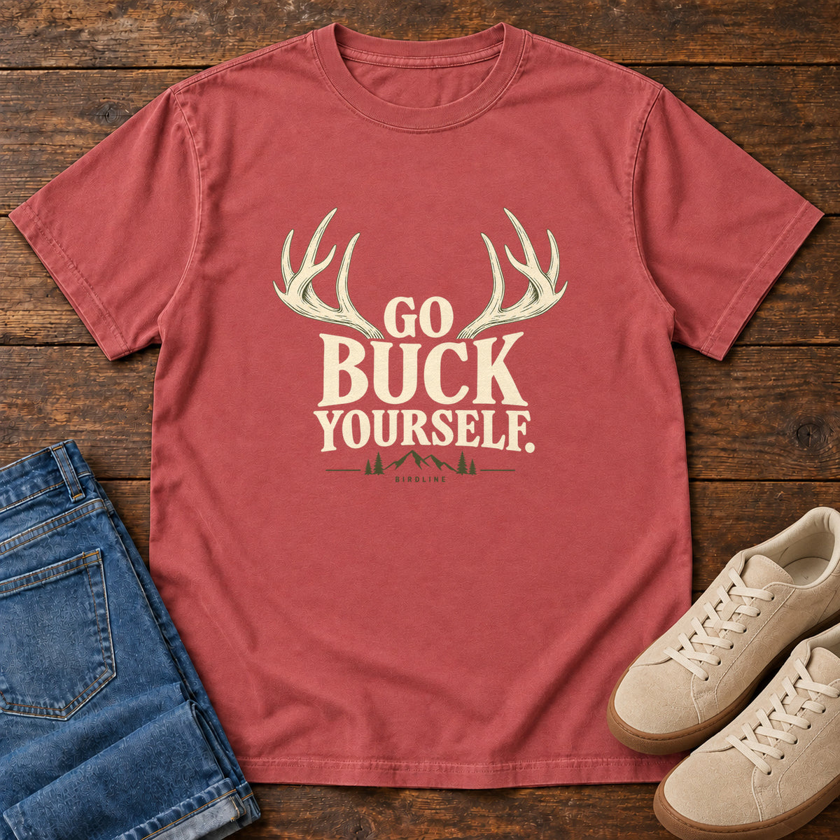 Crimson Go Buck Yourself T-Shirt with cream deer antlers framing Go Buck Yourself lettering, front flat lay on wood.