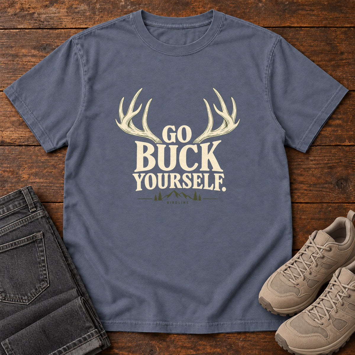 Denim Go Buck Yourself T-Shirt with cream deer antlers framing Go Buck Yourself lettering, front flat lay on wood.