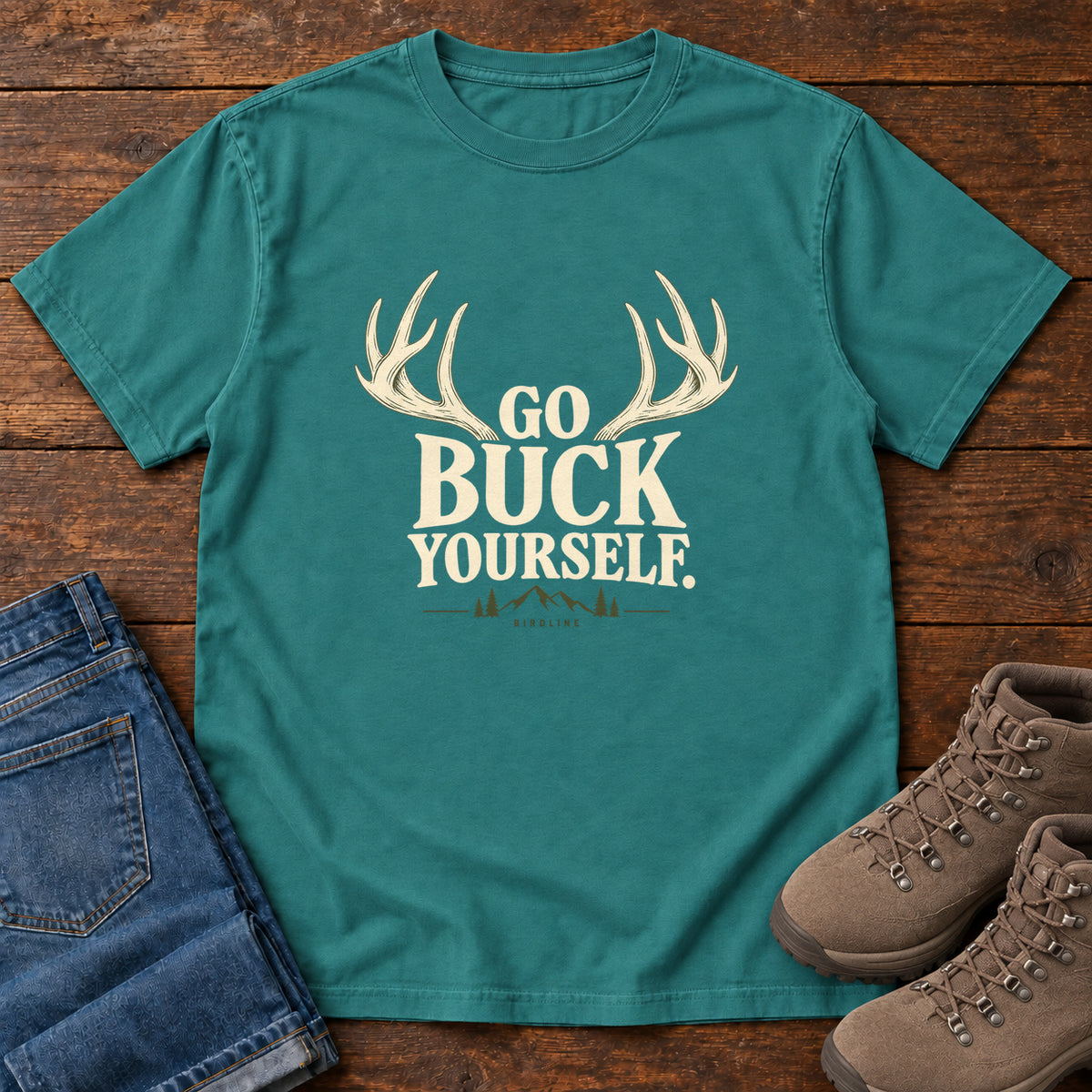 Emerald Go Buck Yourself T-Shirt with cream deer antlers framing Go Buck Yourself lettering, front flat lay on wood.