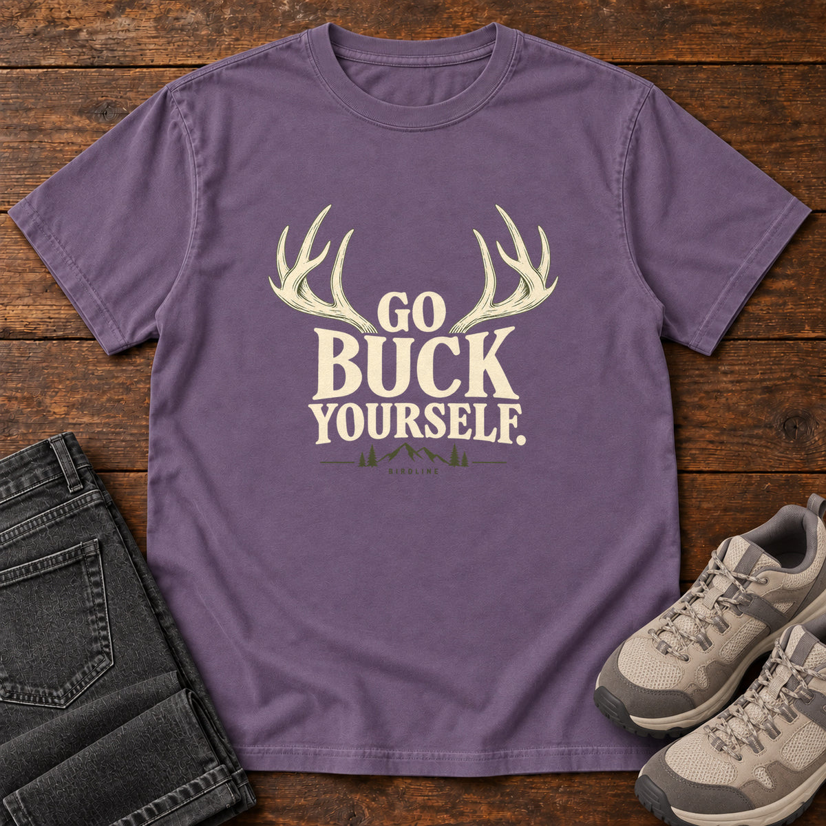 Grape Go Buck Yourself T-Shirt with cream deer antlers framing Go Buck Yourself lettering, front flat lay on wood.