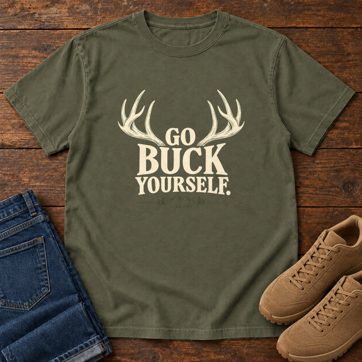 Sage Go Buck Yourself T-Shirt with cream deer antlers framing Go Buck Yourself lettering, front flat lay on wood.