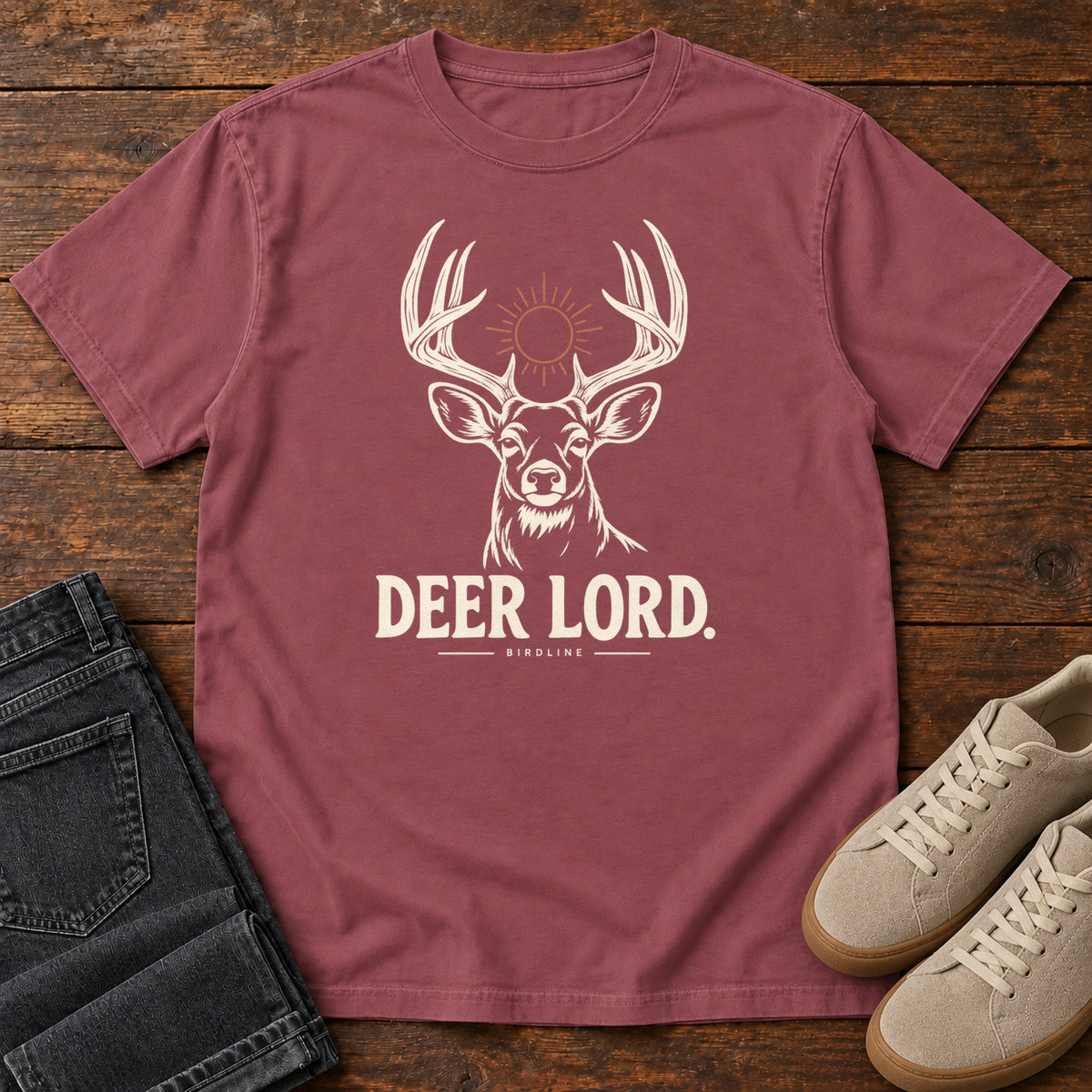 Brick Deer Lord T-Shirt with a cream antlered deer head, a sun symbol and Deer Lord lettering; front flat lay on wood.