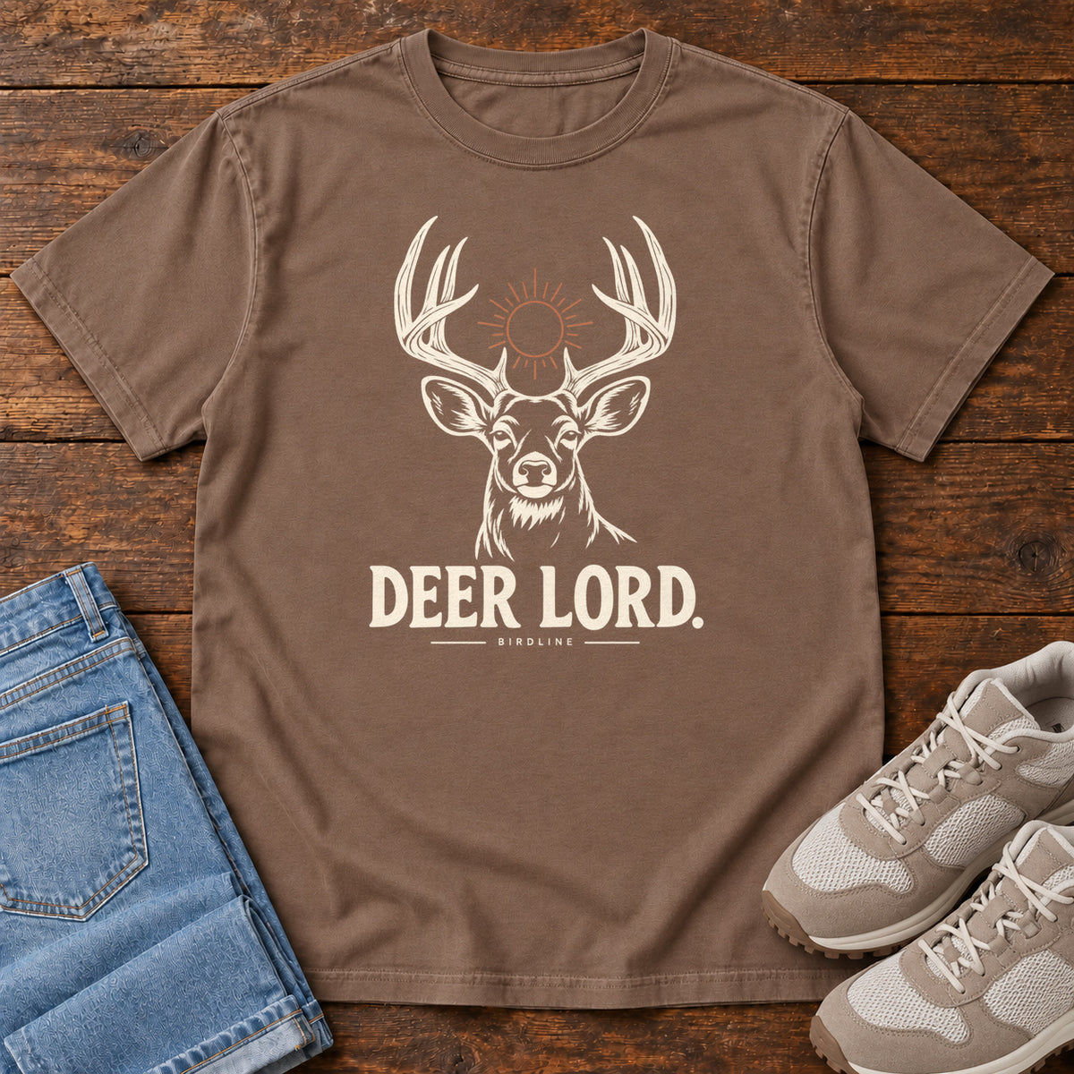 Espresso Deer Lord T-Shirt with a cream antlered deer head, a sun symbol and Deer Lord lettering; front flat lay on wood.