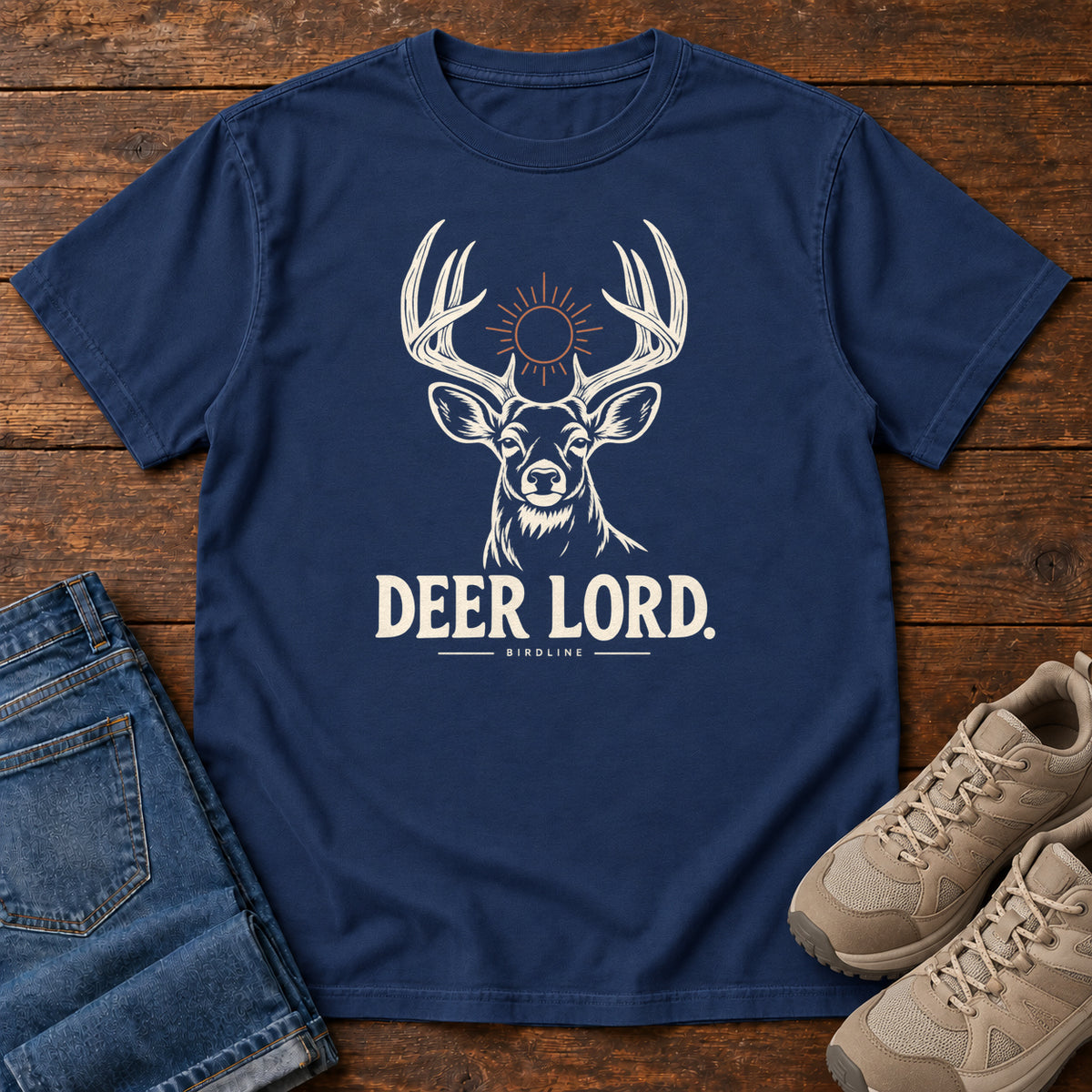 True Navy Deer Lord T-Shirt with a cream antlered deer head, a sun symbol and Deer Lord lettering; front flat lay on wood.