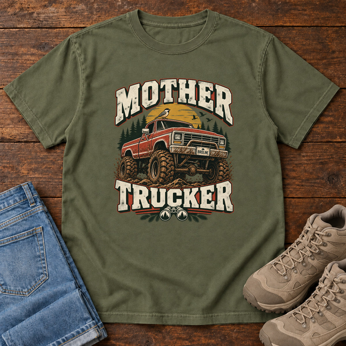Hemp Mother Trucker Red Truck T-Shirt with a lifted red pickup truck, evergreen trees and cream lettering, front flat lay on wood.