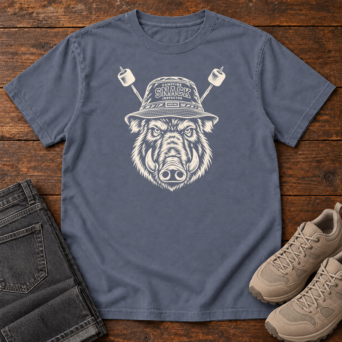 Snack Patrol Boar T-Shirt in Denim, front laid flat on wood, featuring a cream boar head wearing a bucket hat, with two marshmallow skewers behind it.
