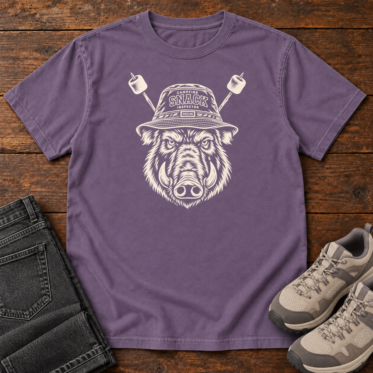 Snack Patrol Boar T-Shirt in Grape, front laid flat on wood, featuring a cream boar head wearing a bucket hat, with two marshmallow skewers behind it.