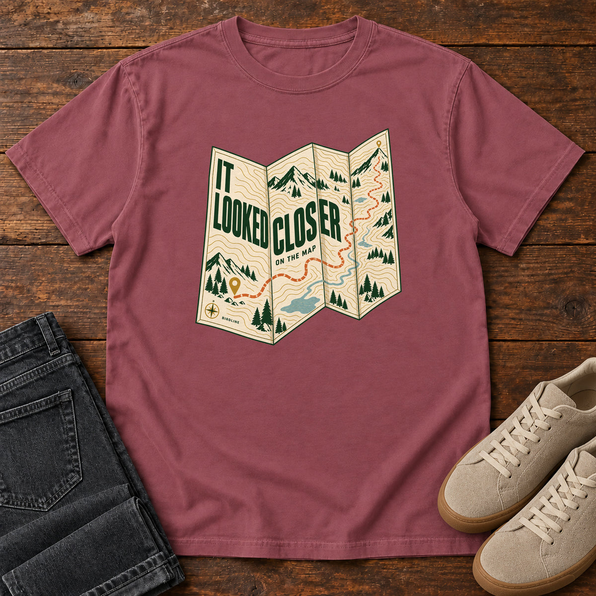 Brick It Looked Closer on the Map T-Shirt with a folded cream map graphic, green lettering and an orange route, front flat lay on wood.
