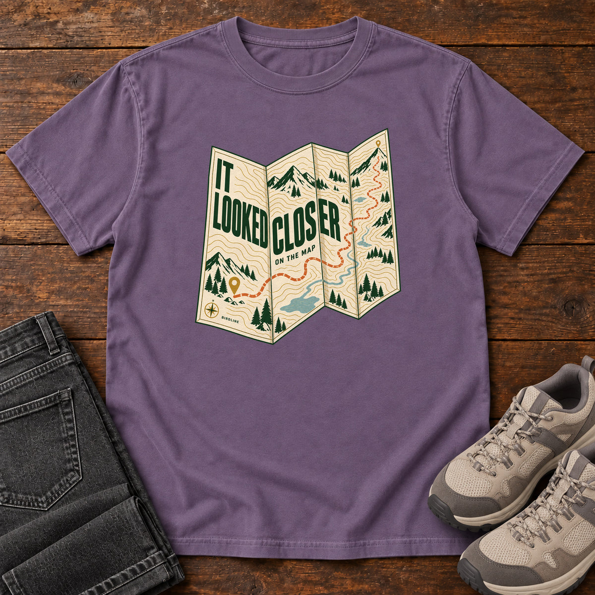 Grape It Looked Closer on the Map T-Shirt with a folded cream map graphic, green lettering and an orange route, front flat lay on wood.