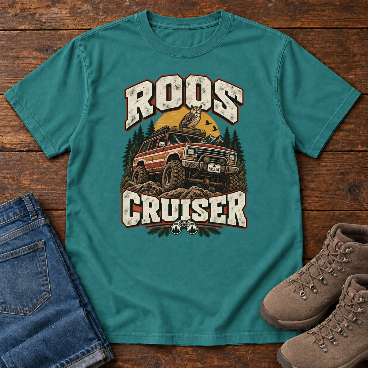 Emerald Roos Cruiser T-Shirt with a bird perched on an off-road vehicle between distressed cream Roos Cruiser lettering, front flat lay on wood.