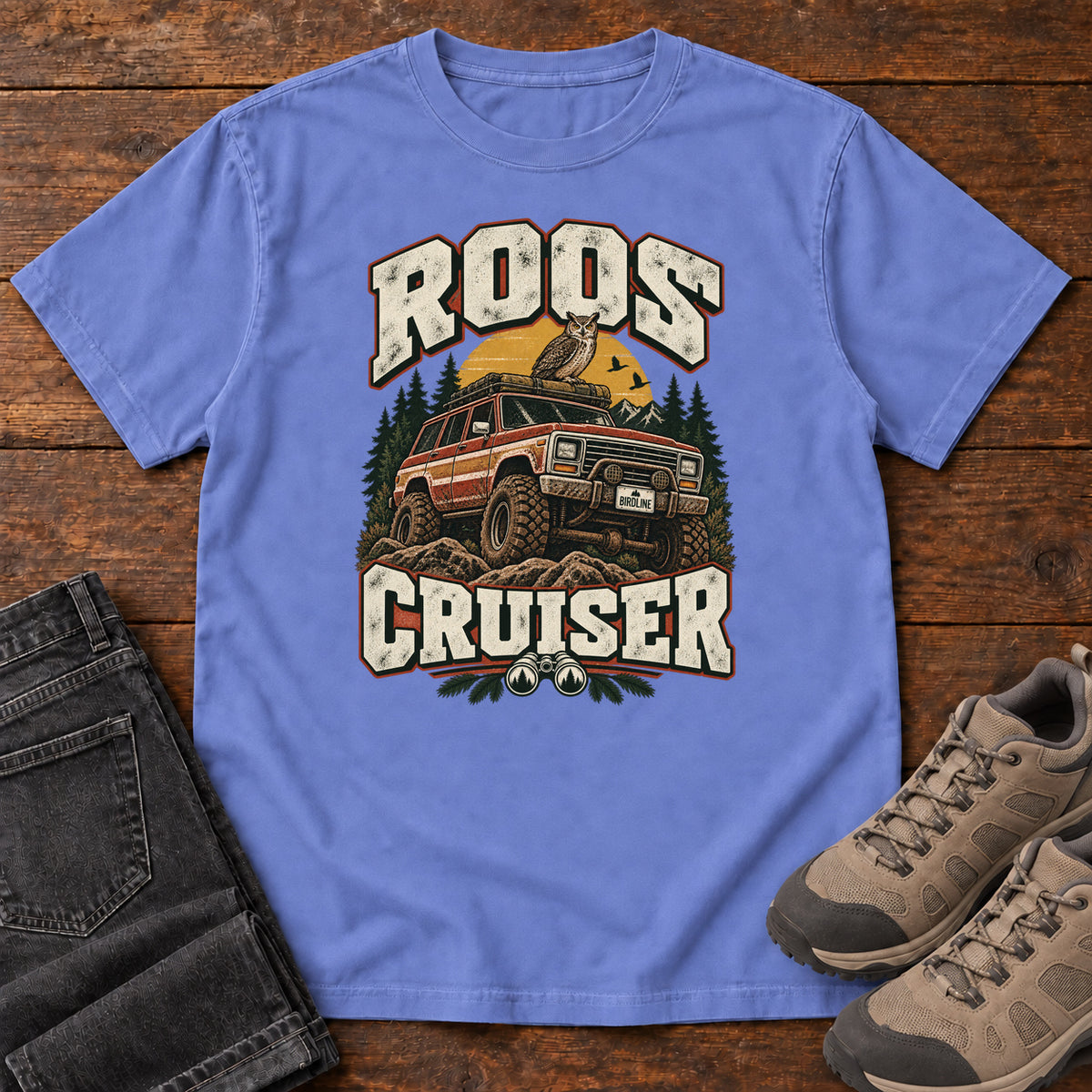 Flo Blue Roos Cruiser T-Shirt with a bird perched on an off-road vehicle between distressed cream Roos Cruiser lettering, front flat lay on wood.