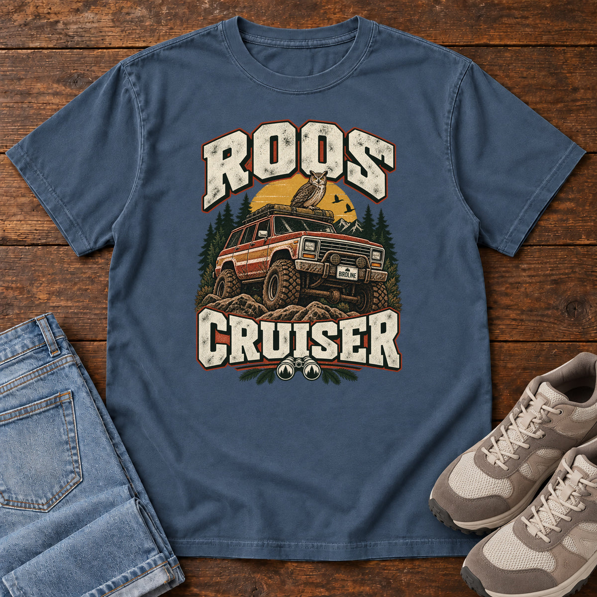 Midnight Roos Cruiser T-Shirt with a bird perched on an off-road vehicle between distressed cream Roos Cruiser lettering, front flat lay on wood.