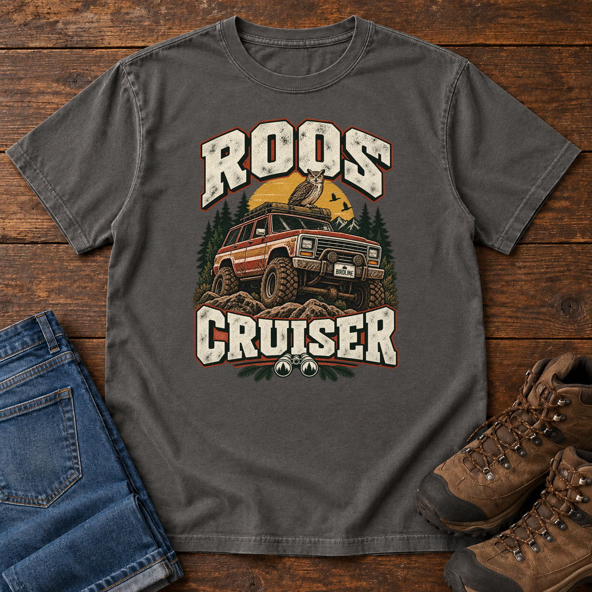 Pepper Roos Cruiser T-Shirt with a bird perched on an off-road vehicle between distressed cream Roos Cruiser lettering, front flat lay on wood.