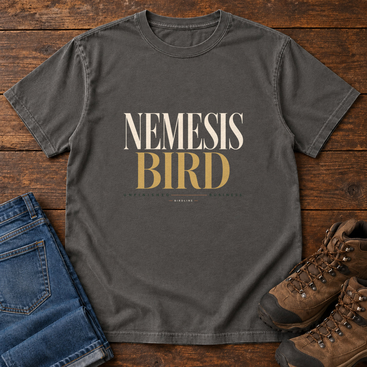 Pepper Nemesis Bird T-Shirt with cream-and-gold serif lettering, front flat lay on wood.