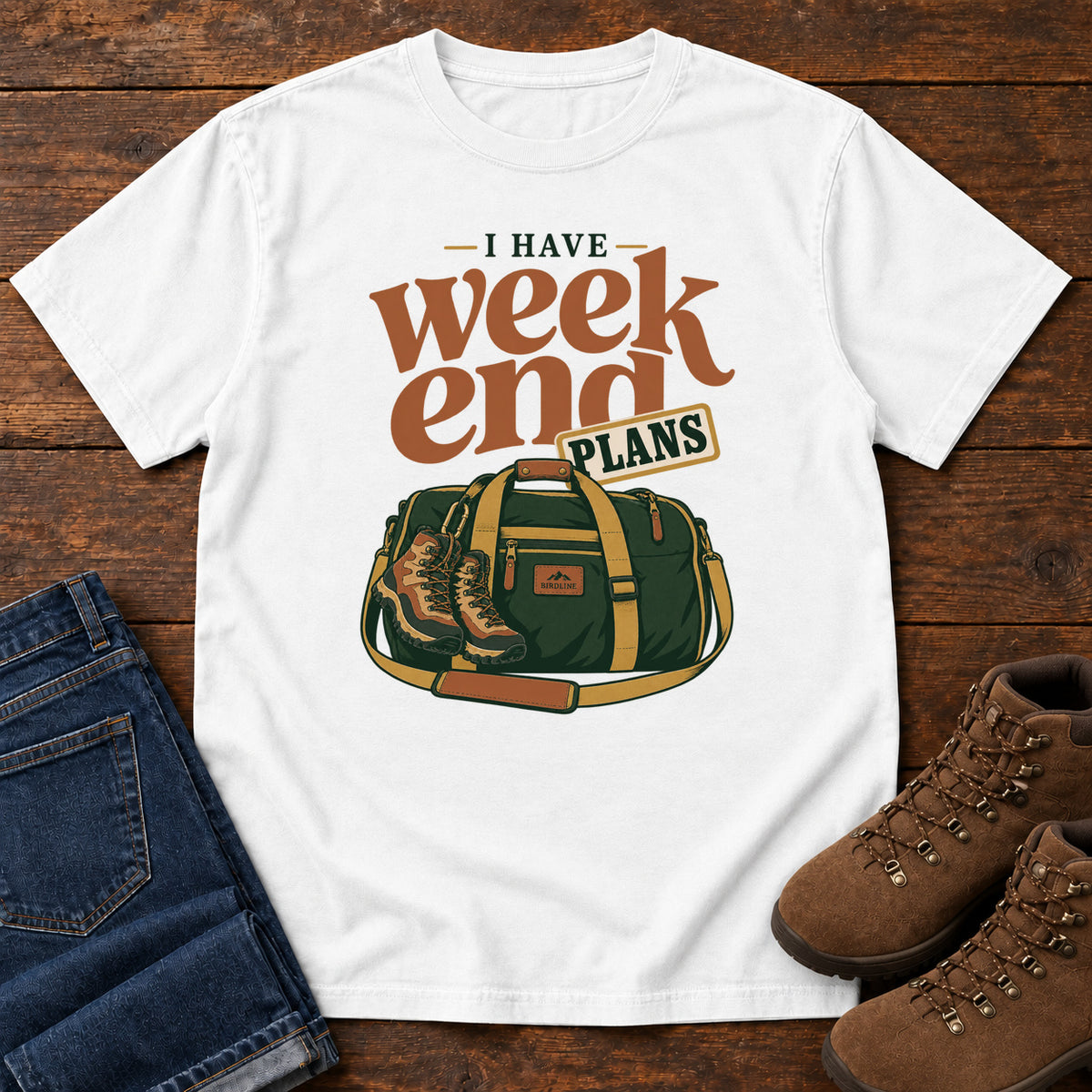 White I Have Weekend Plans T-Shirt with a green duffel bag and hiking boots beneath rust-orange Weekend lettering, front flat lay on wood.