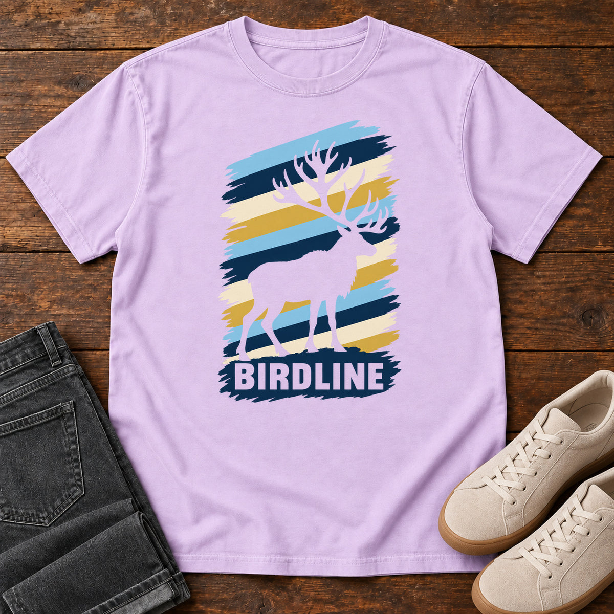 Birdline Elk Stripes T-Shirt in Orchid, front laid flat on wood, featuring an elk silhouette against blue, cream and gold brushstroke stripes above BIRDLINE lettering.