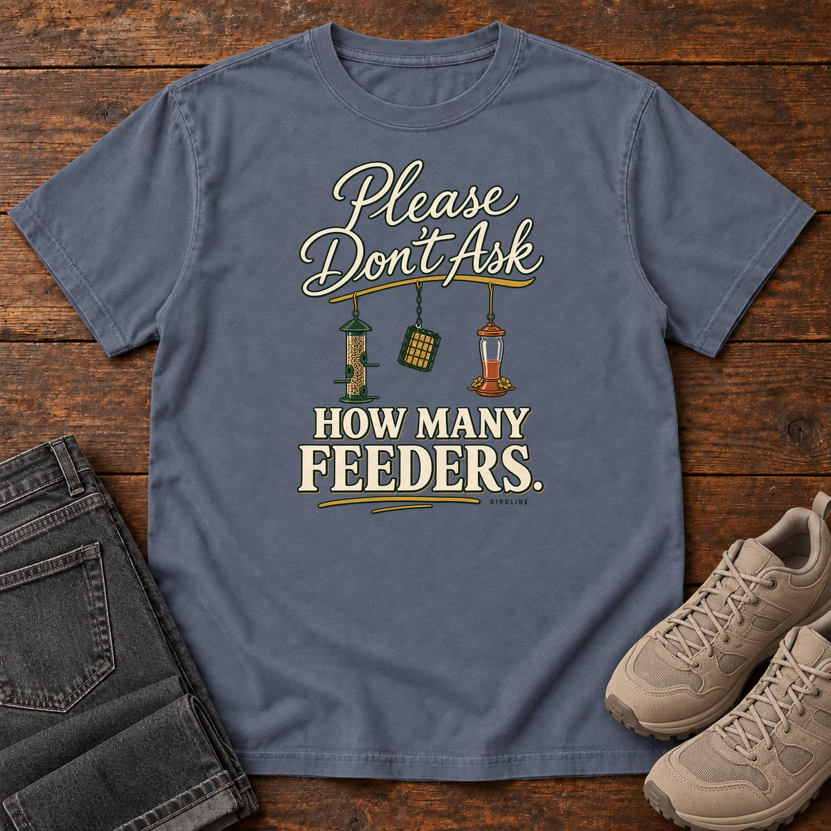 Denim Please Don't Ask How Many Feeders T-Shirt with cream lettering and three hanging bird feeders, front flat lay on wood.