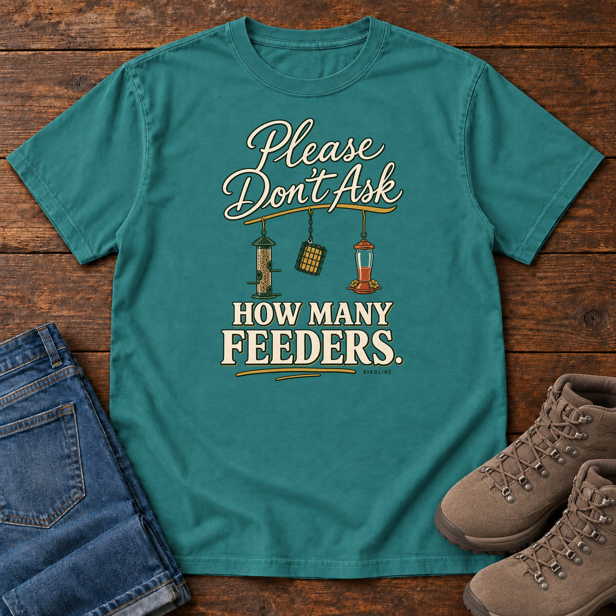 Emerald Please Don't Ask How Many Feeders T-Shirt with cream lettering and three hanging bird feeders, front flat lay on wood.