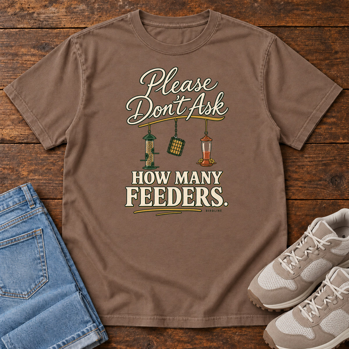 Espresso Please Don't Ask How Many Feeders T-Shirt with cream lettering and three hanging bird feeders, front flat lay on wood.