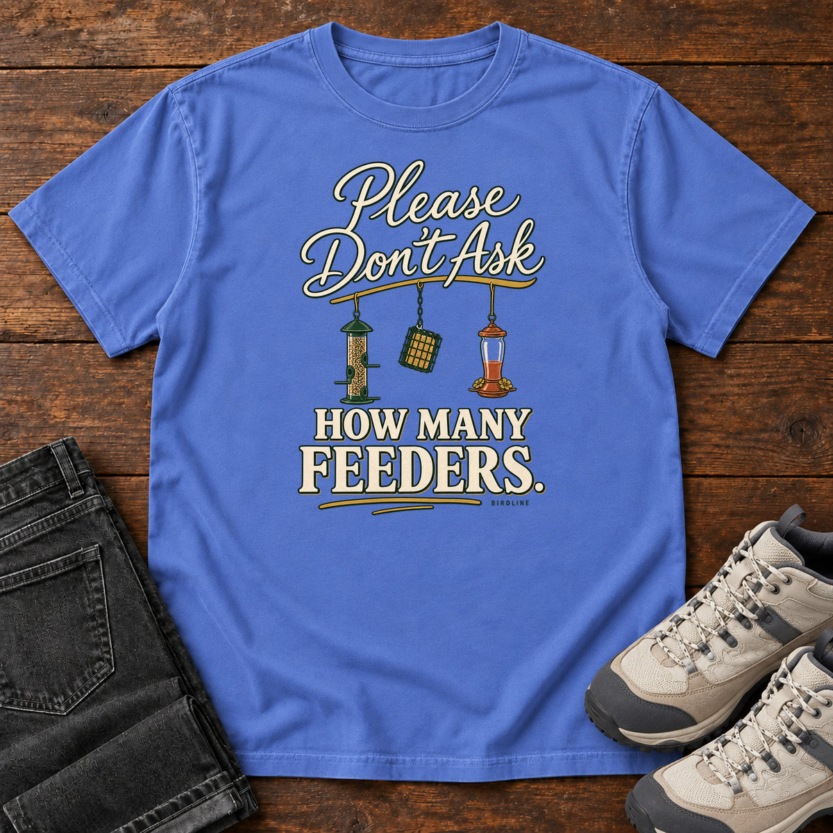 Mystic Blue Please Don't Ask How Many Feeders T-Shirt with cream lettering and three hanging bird feeders, front flat lay on wood.