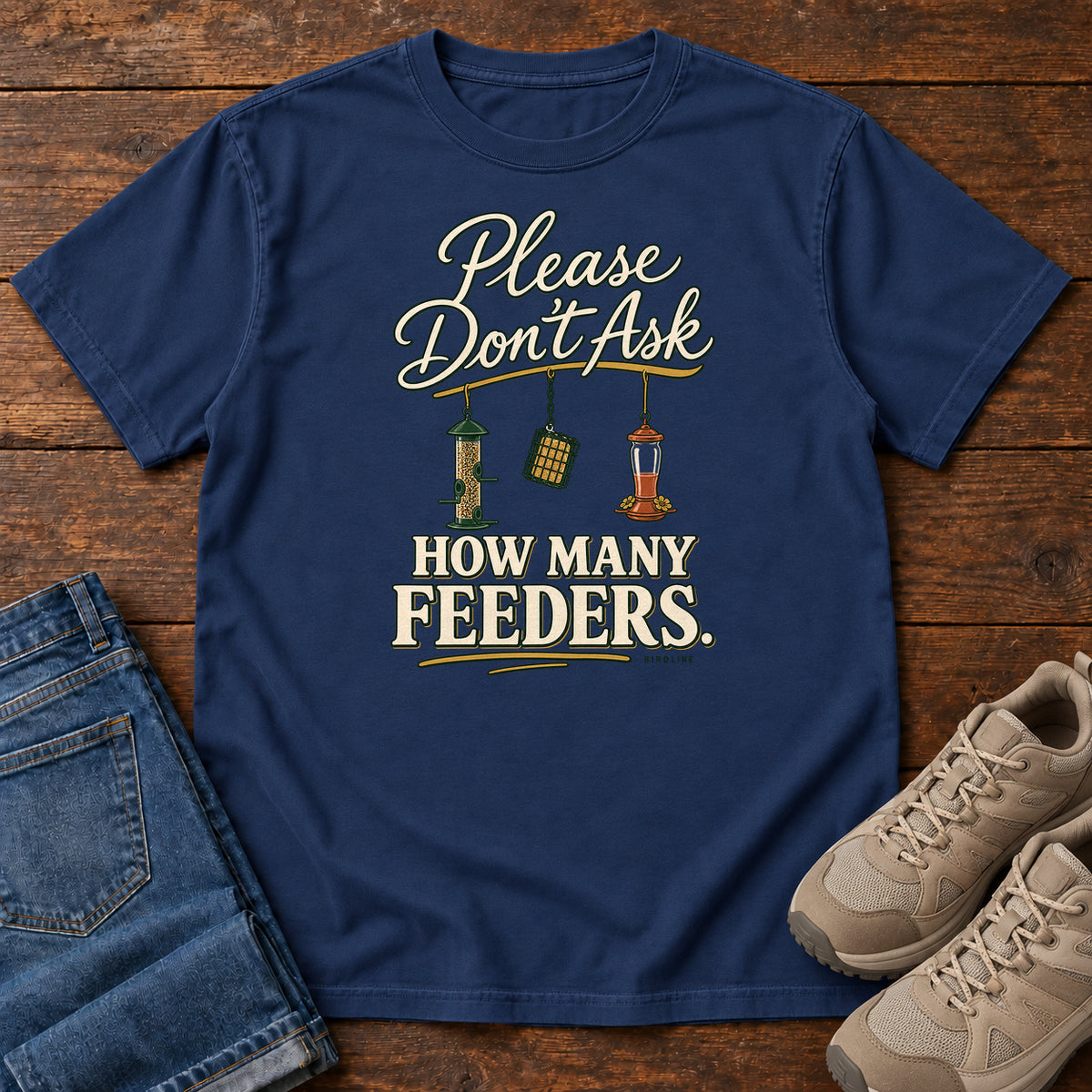 True Navy Please Don't Ask How Many Feeders T-Shirt with cream lettering and three hanging bird feeders, front flat lay on wood.