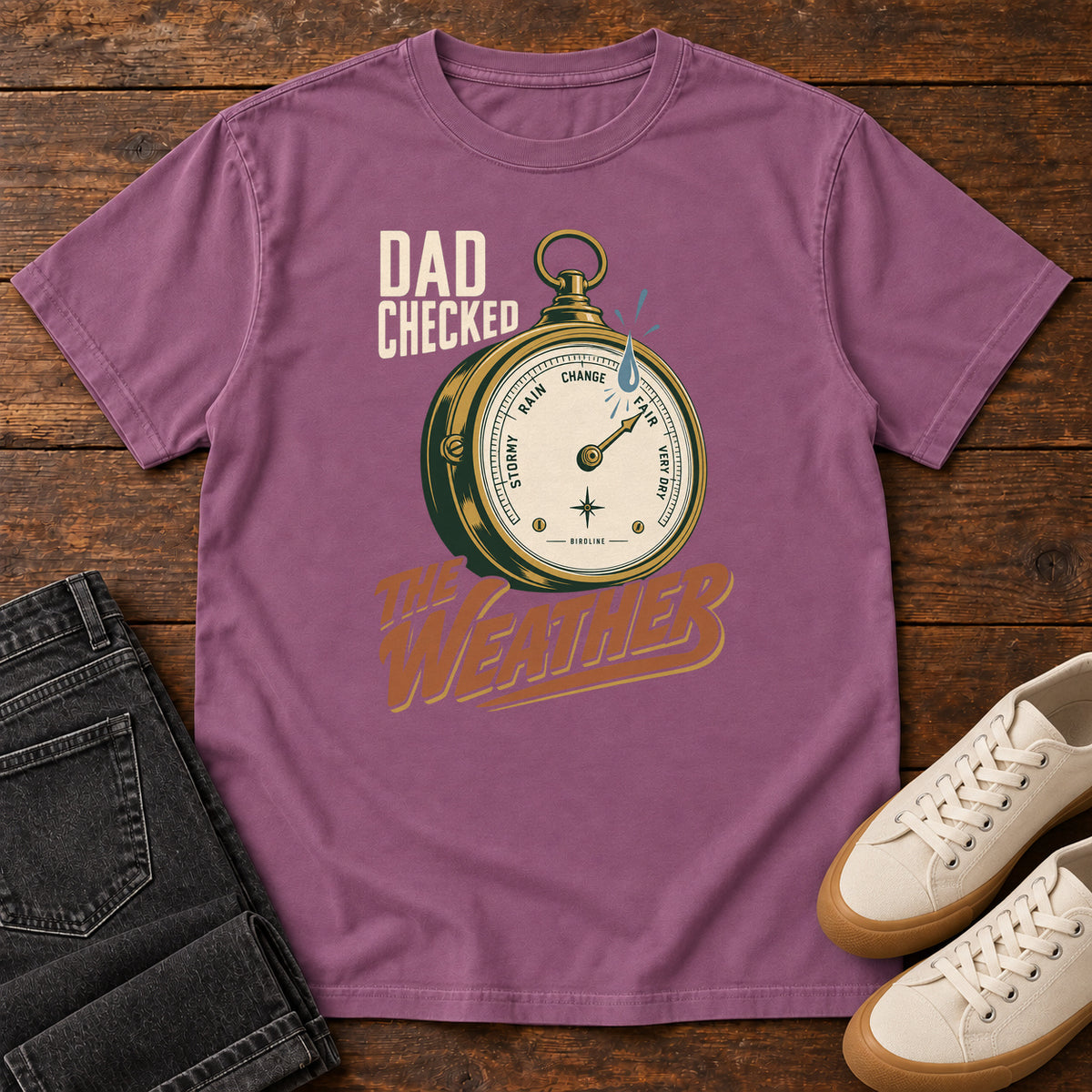 Berry Dad Checked the Weather T-shirt with a weather dial graphic and lettering, laid flat on a wooden surface.