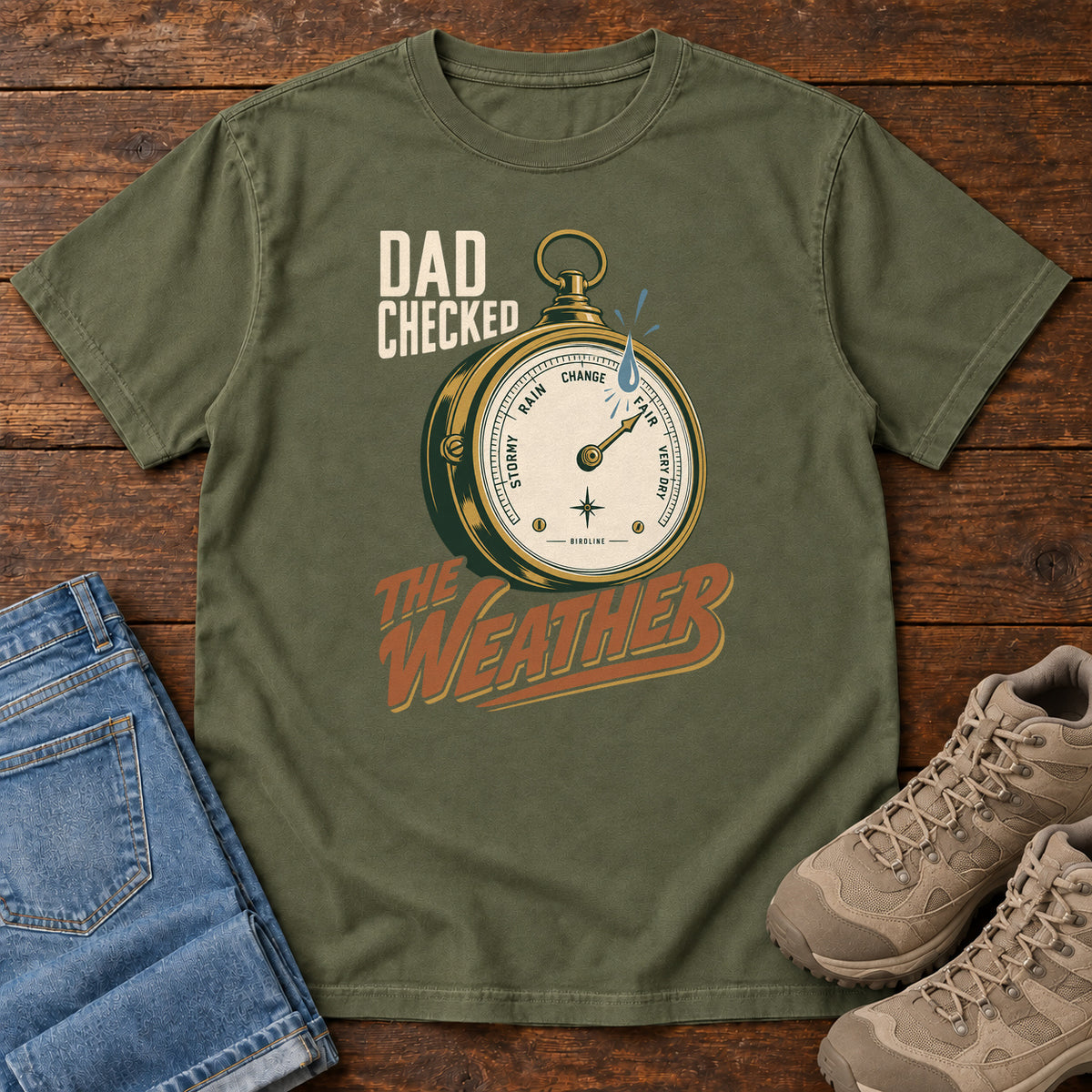 Hemp Dad Checked the Weather T-shirt with a weather dial graphic and lettering, laid flat on a wooden surface.