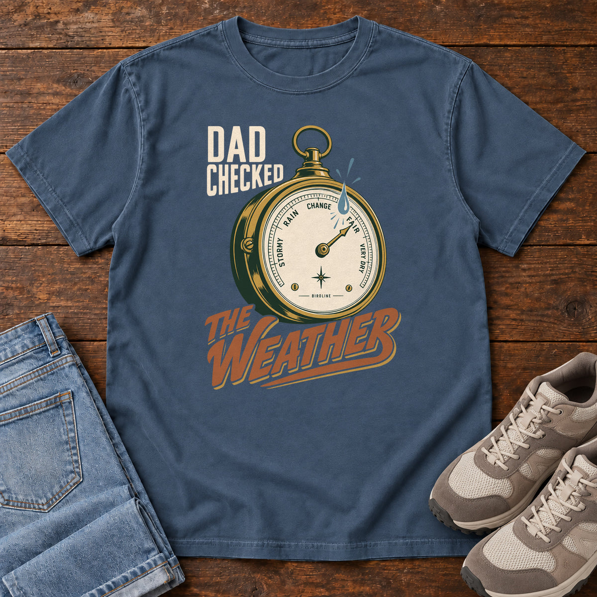 Midnight Dad Checked the Weather T-shirt with a weather dial graphic and lettering, laid flat on a wooden surface.