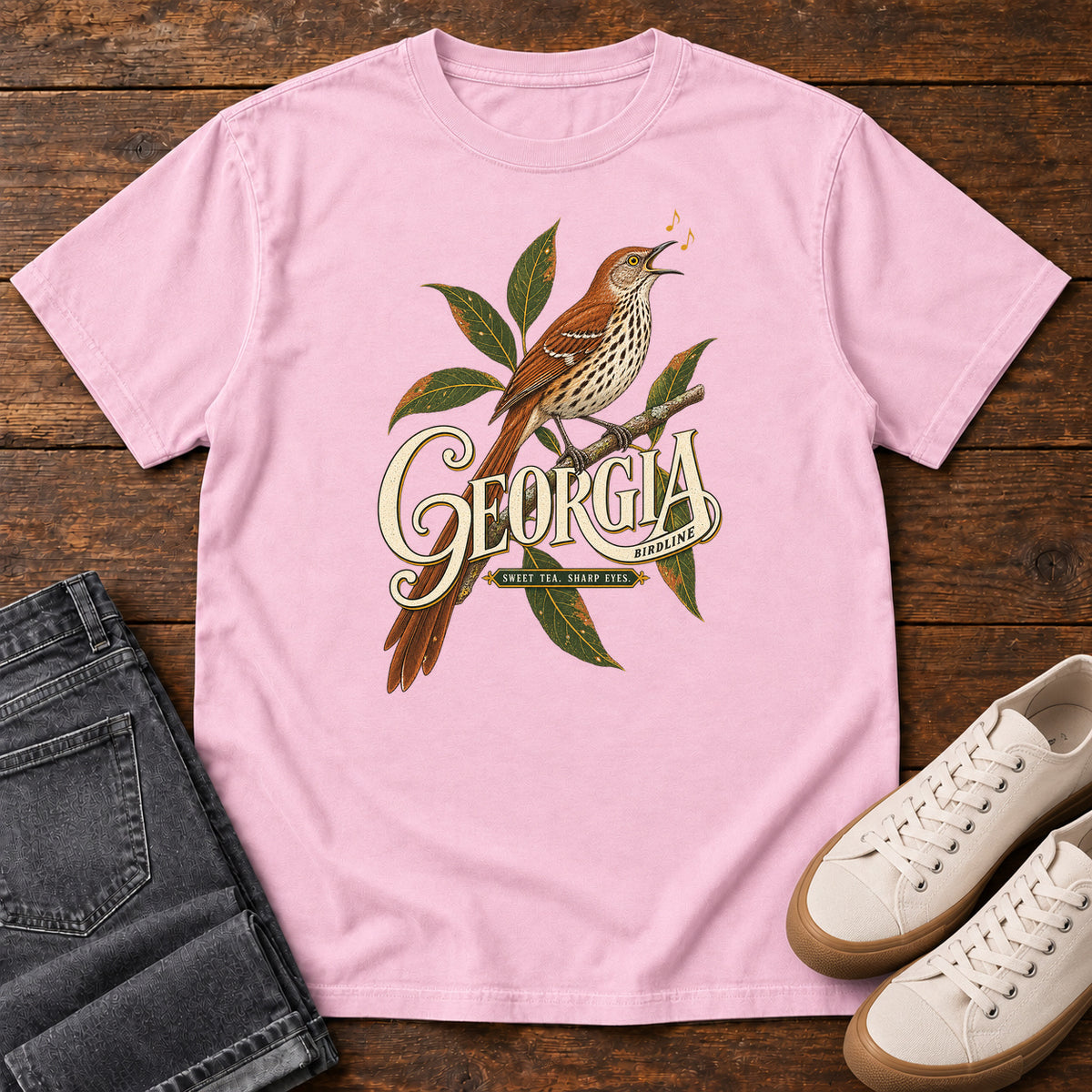 Blossom Georgia Sharp Eyes T-Shirt with a brown, speckle-breasted bird on a leafy branch above Georgia lettering, front flat lay on wood.