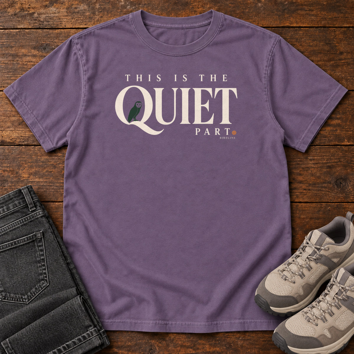Grape This Is the Quiet Part T-Shirt with cream This Is the Quiet Part lettering with a small green bird inside the Q, front flat lay on wood.