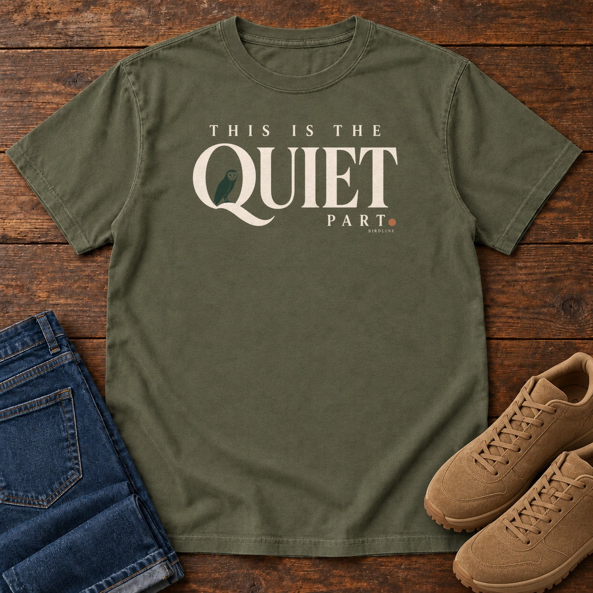 Sage This Is the Quiet Part T-Shirt with cream This Is the Quiet Part lettering with a small green bird inside the Q, front flat lay on wood.