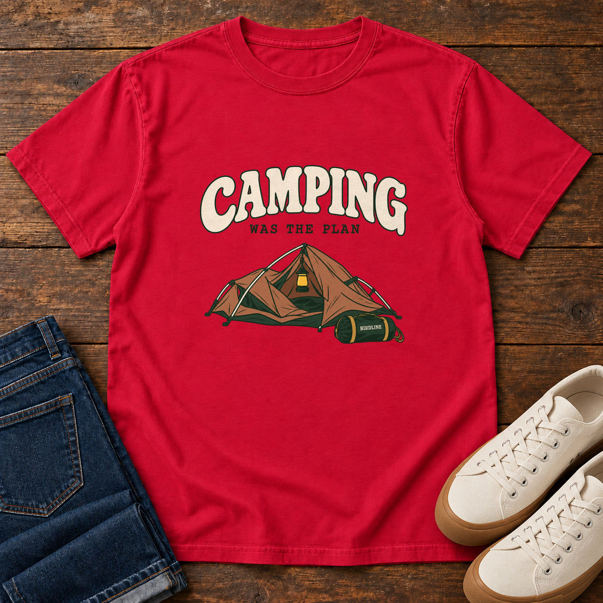 Red Camping Was the Plan T-Shirt with an orange tent with a hanging lantern and green gear bag; front flat lay on wood.