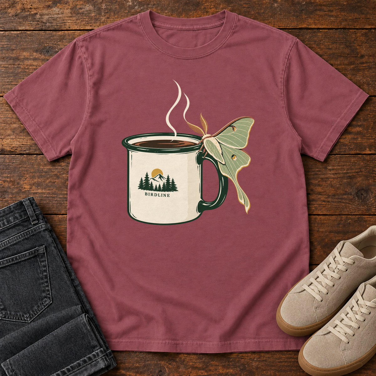 Brick Coffee and Luna Moth T-Shirt with a steaming cream camp mug with green trim and a pale green long-tailed moth; front flat lay on wood.