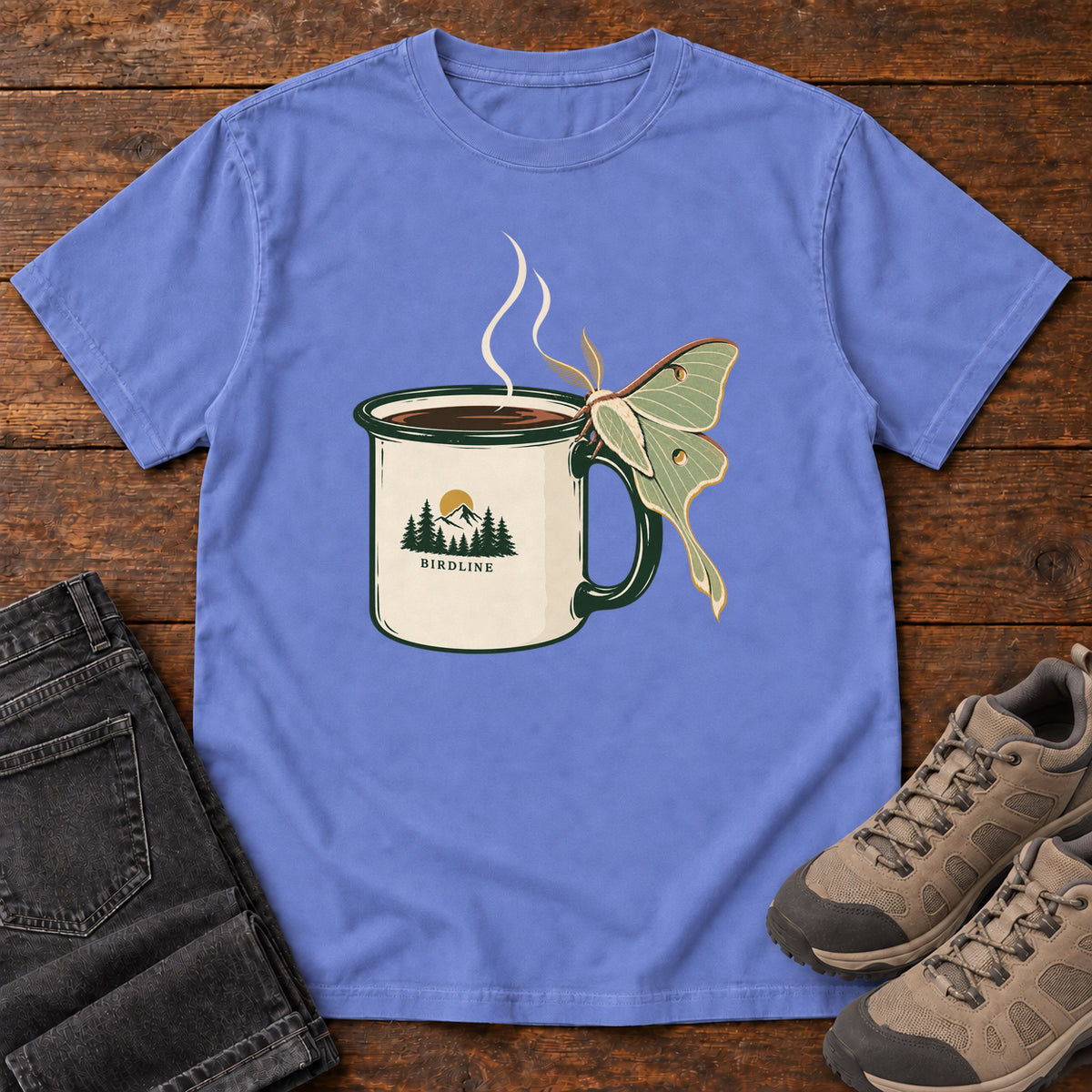 Flo Blue Coffee and Luna Moth T-Shirt with a steaming cream camp mug with green trim and a pale green long-tailed moth; front flat lay on wood.