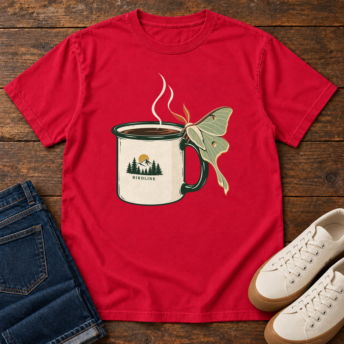 Red Coffee and Luna Moth T-Shirt with a steaming cream camp mug with green trim and a pale green long-tailed moth; front flat lay on wood.