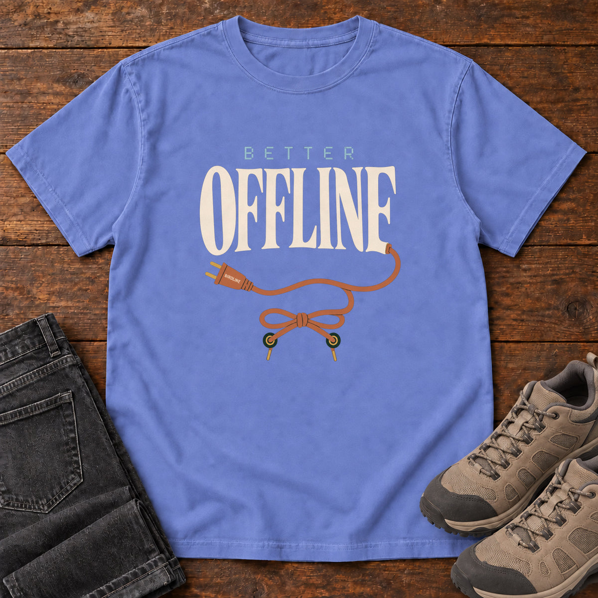 Flo Blue Better Offline T-Shirt with cream Better Offline lettering and an orange unplugged cord; front flat lay on wood.